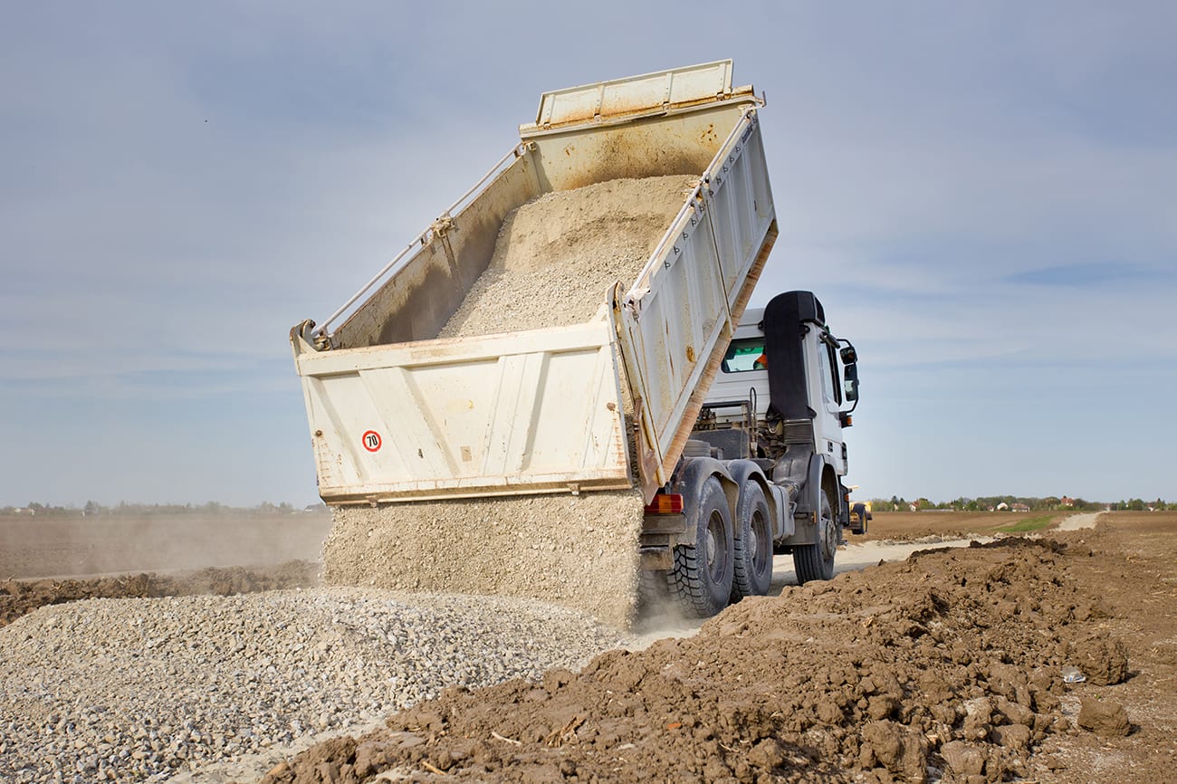 Tipping truck unloading gravel on road construction site